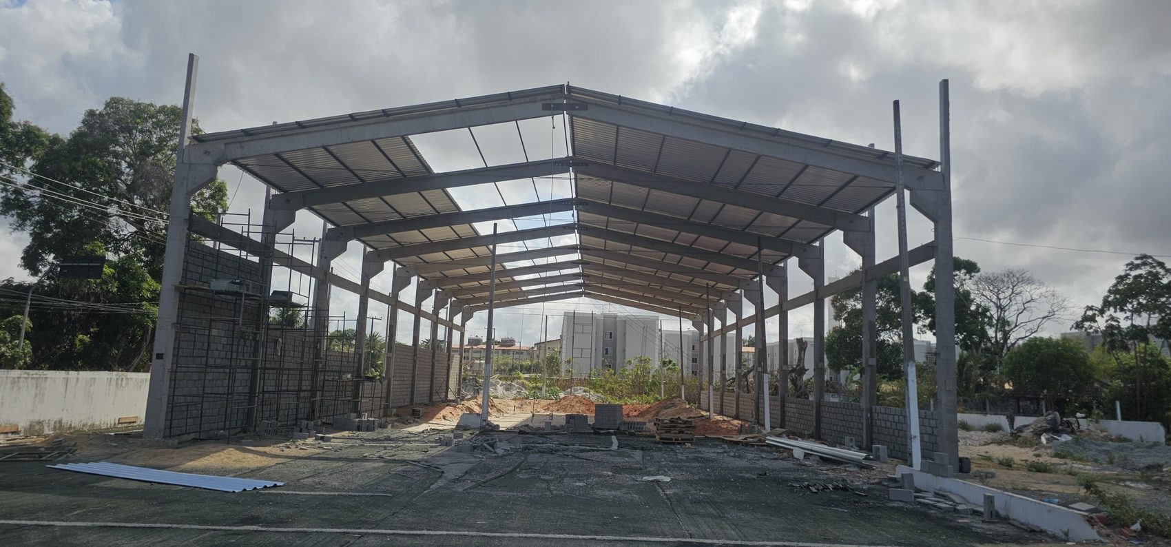Galpão com pórticos pré-fabricados concluídos e cobertura metálica sendo instalada