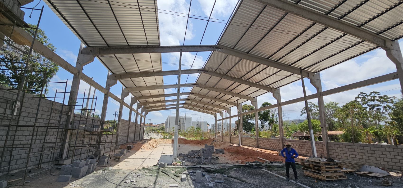 Interior do galpão pré-fabricado em execução, com pórticos de concreto e cobertura metálica
