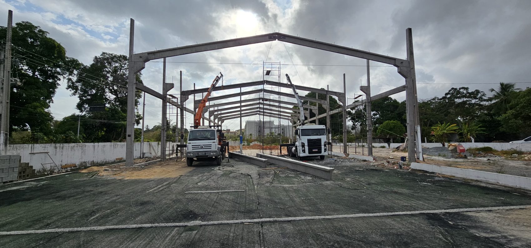 Dois caminhões munck montando os pórticos pré-fabricados do galpão em obra
