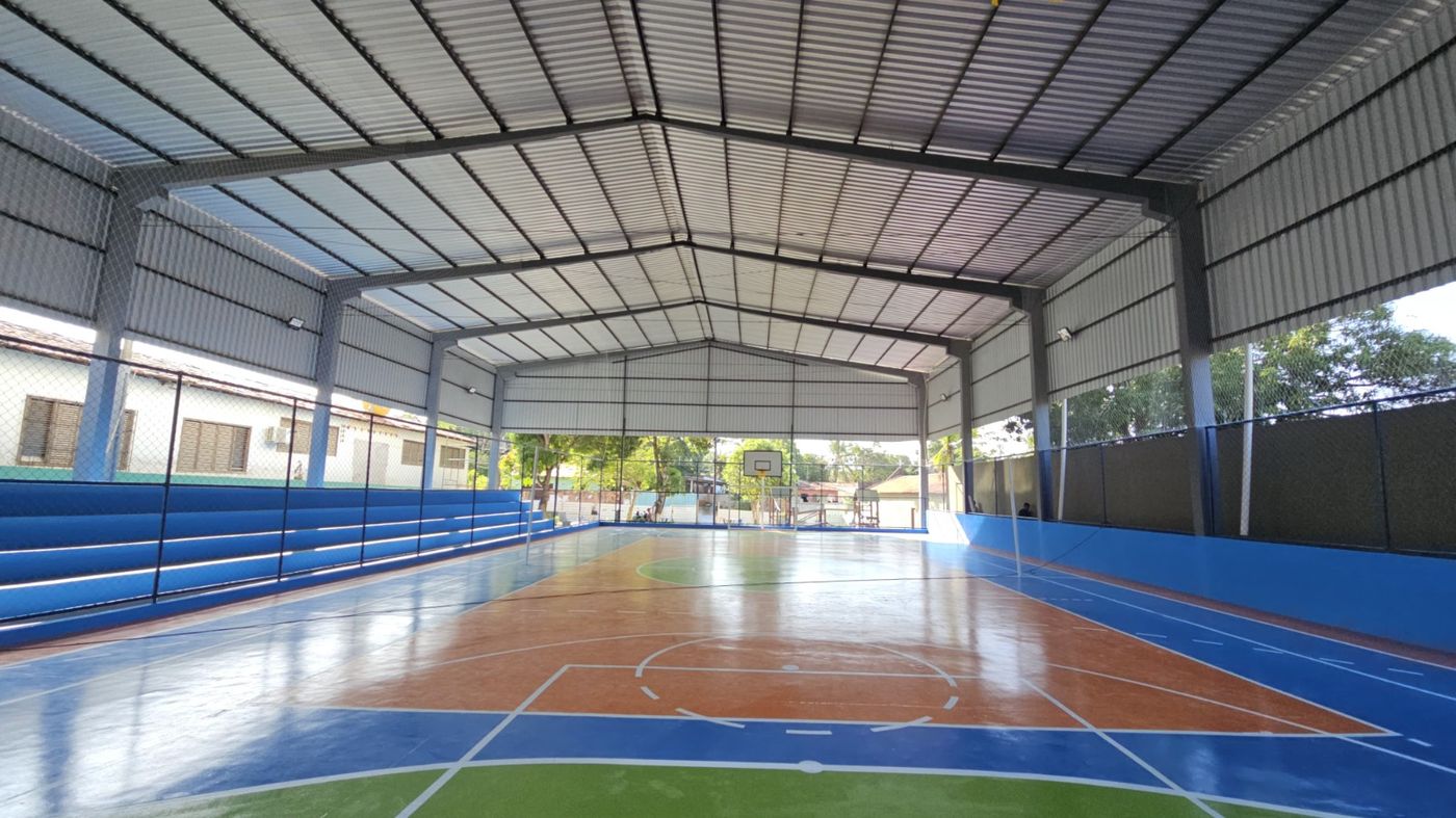 Quadra poliesportiva coberta concluída, com arquibancada, alambrado e piso pintado